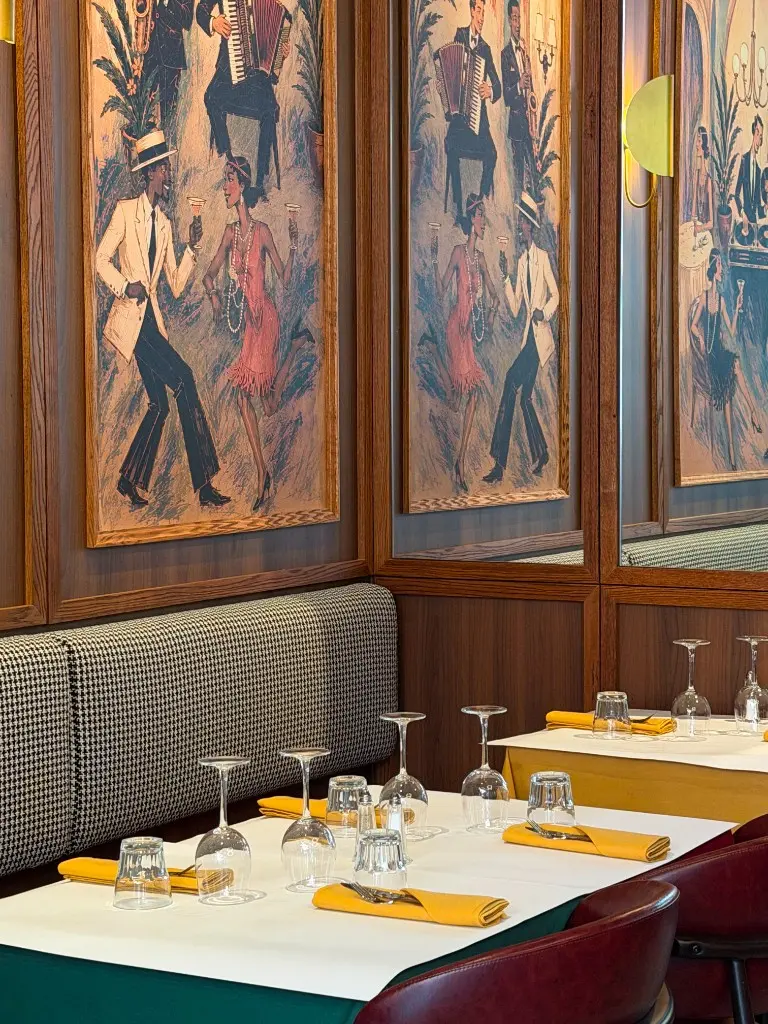 Entrecôte dining tables beside framed Parisian artwork and wood paneling
